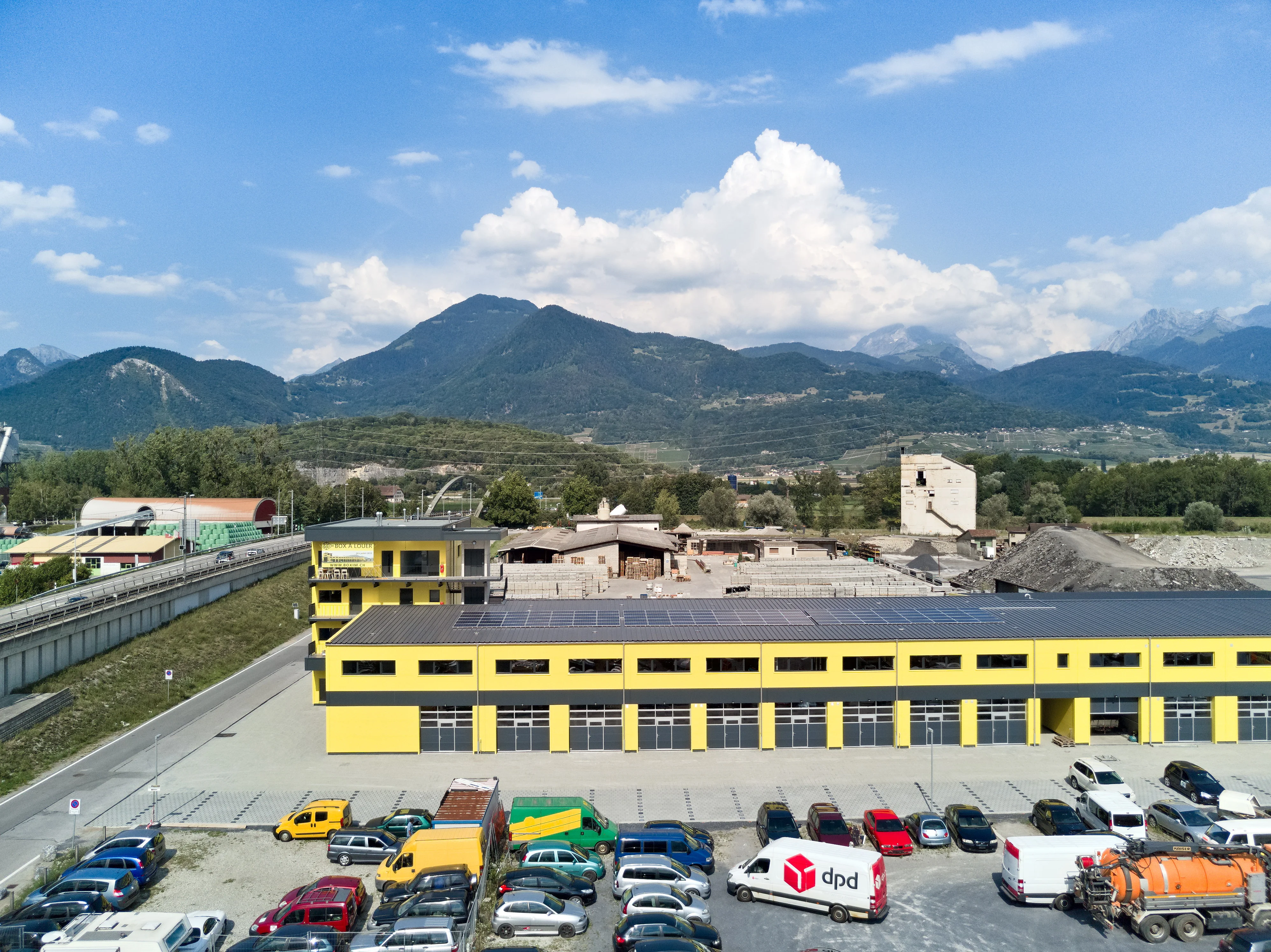 Photo BOXIM, Ensemble de halls à louer modulables, à l’entrée de Monthey, à la structure métallique contemporaine et à la façade jaune identitaire.